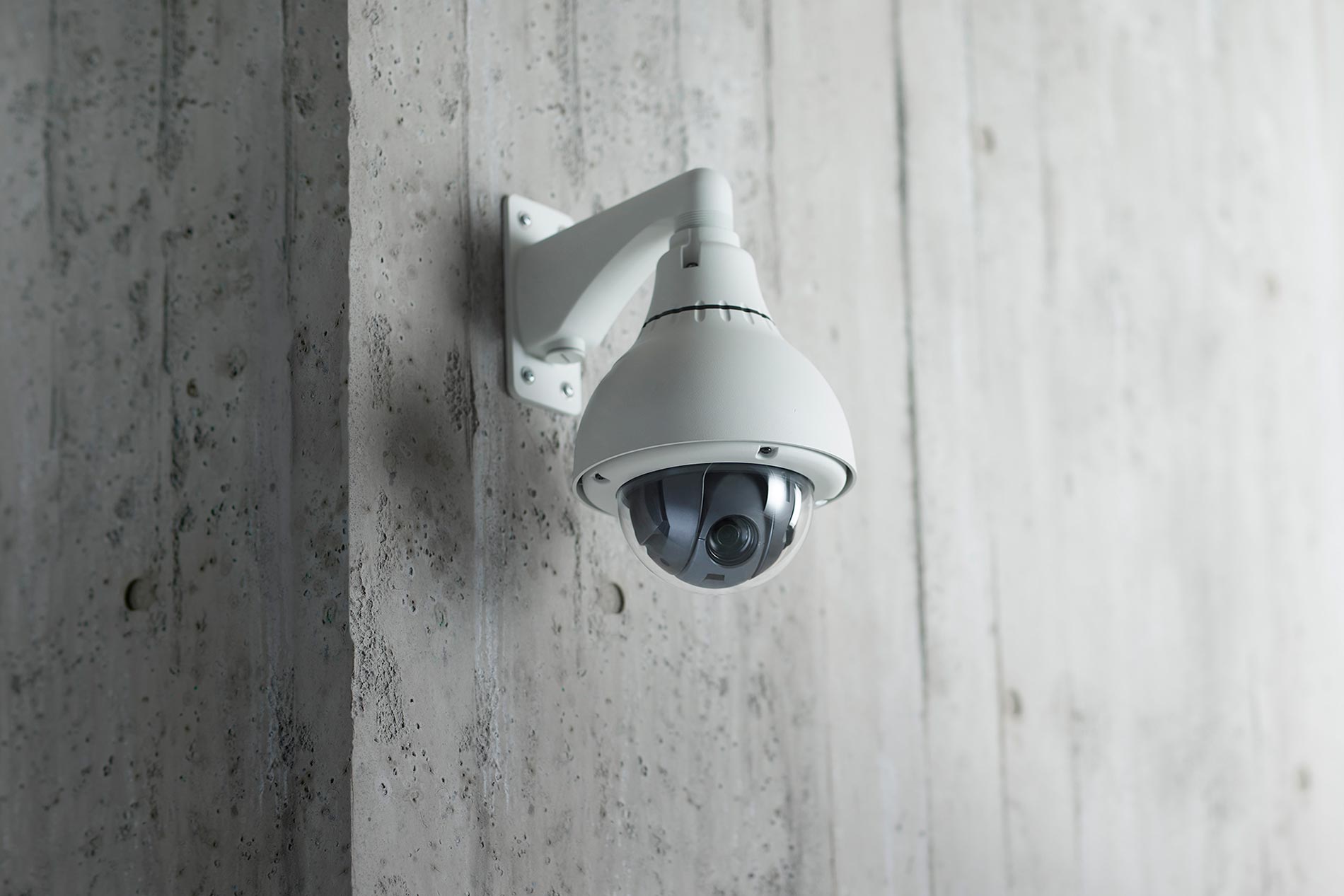 A technician installing outdoor surveillance cameras on a white wall near a warehouse door.
