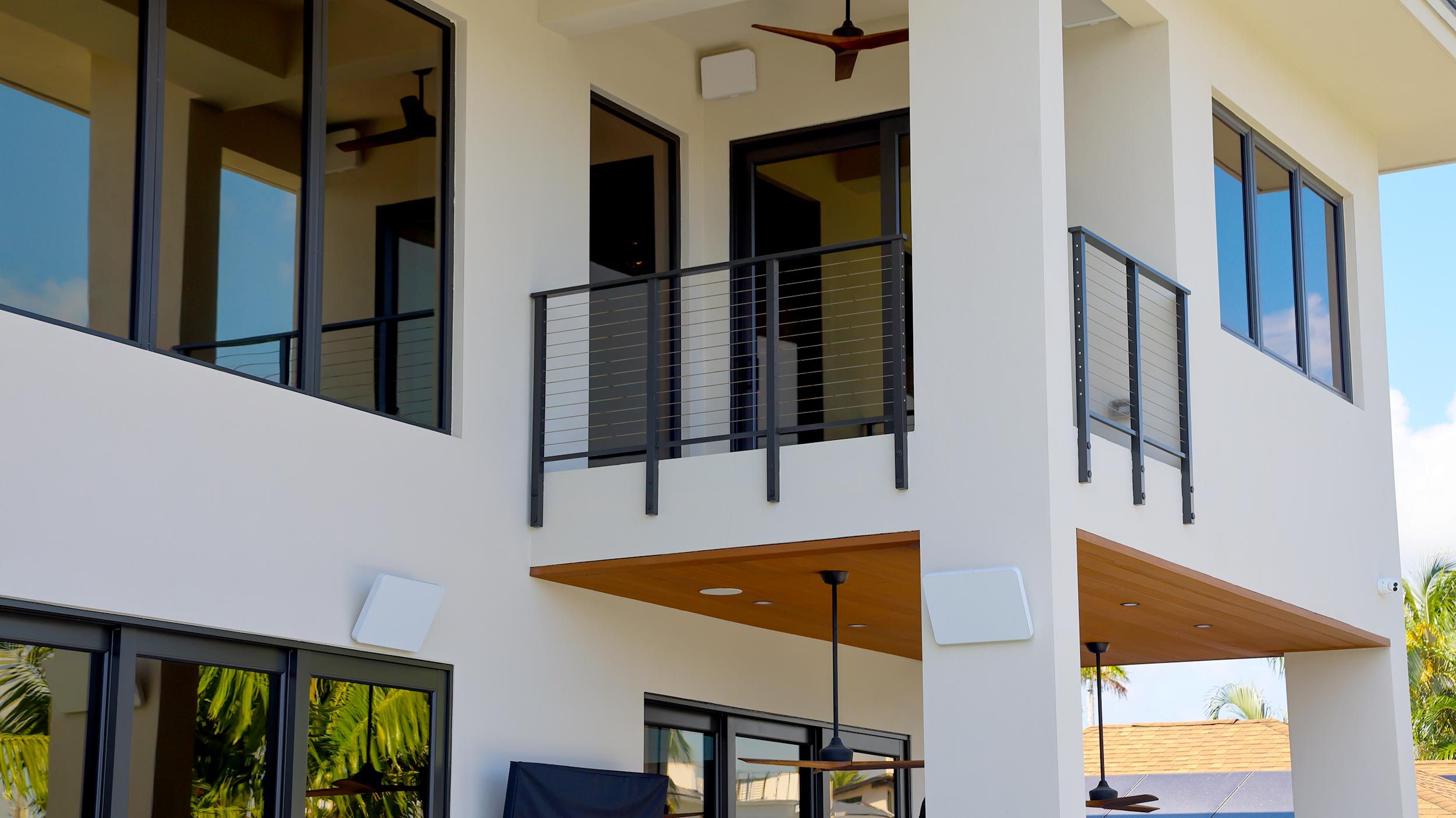 A two-story modern home with a balcony, outdoor speakers, and clean architectural lines.